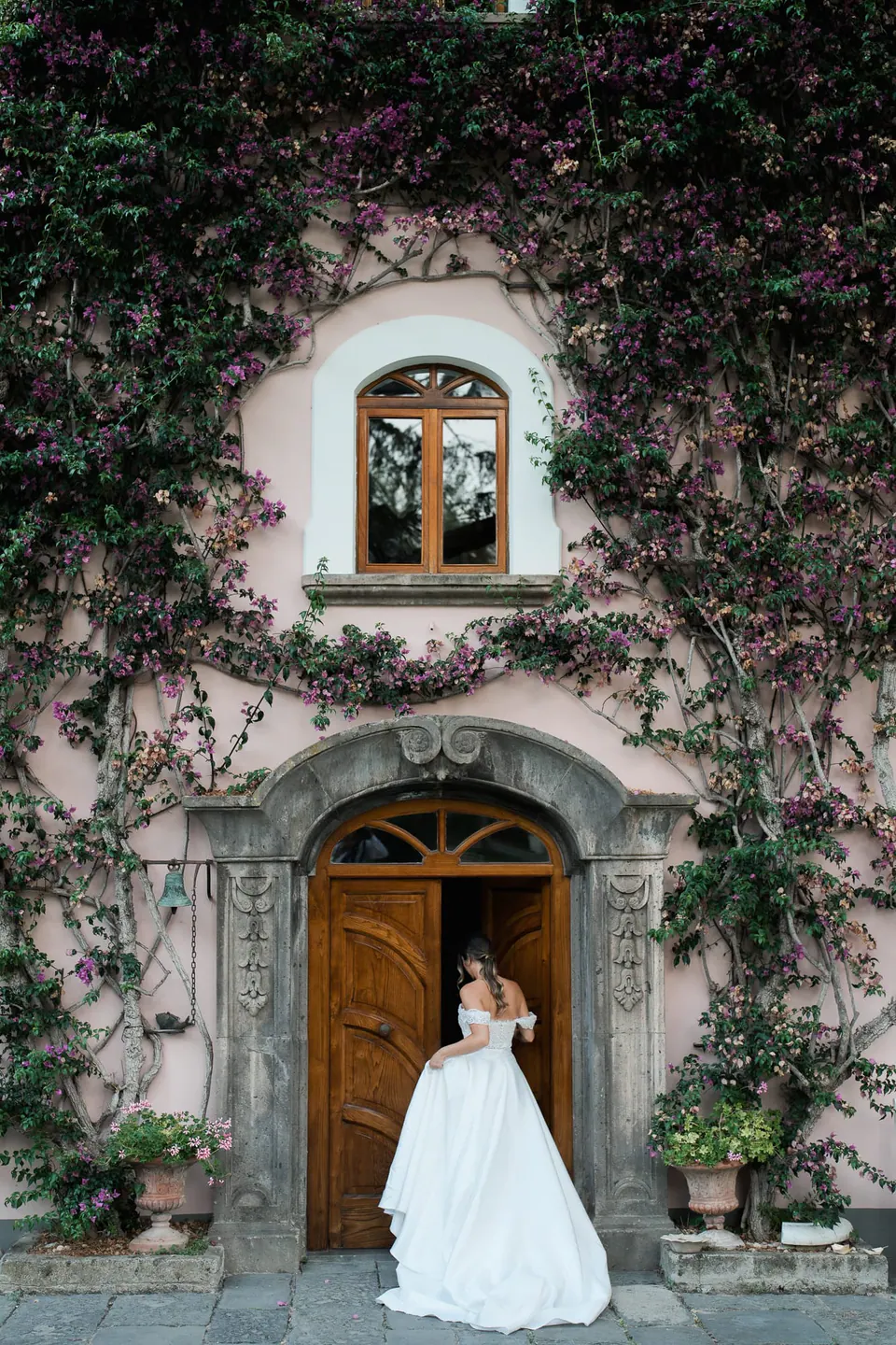 Bride at the arched wooden door of the pink, ivy-covered villa of Capo Santa Fortunata.