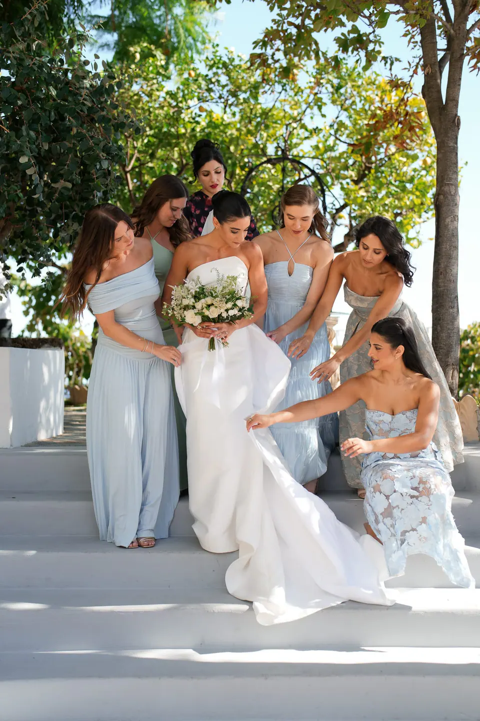 Bridesmaids in powder blue helping the bride on the white steps.