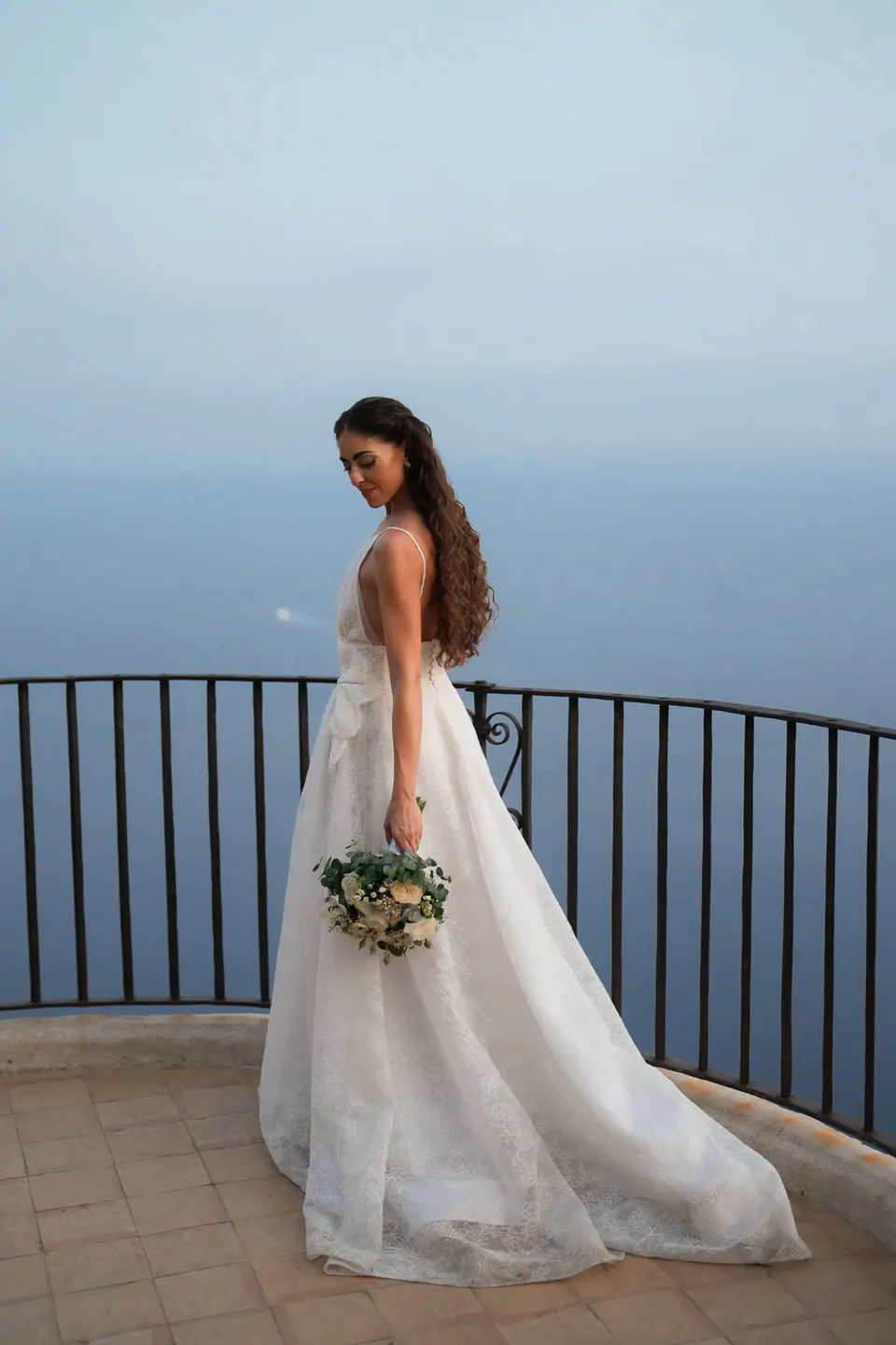Bride at the railing high above the sea, her train spread on the terrace.