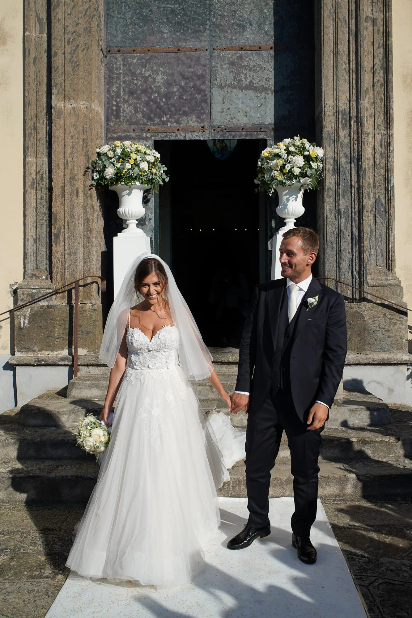 Bride and groom at the church door between white flowers before the Relais Blu celebration.