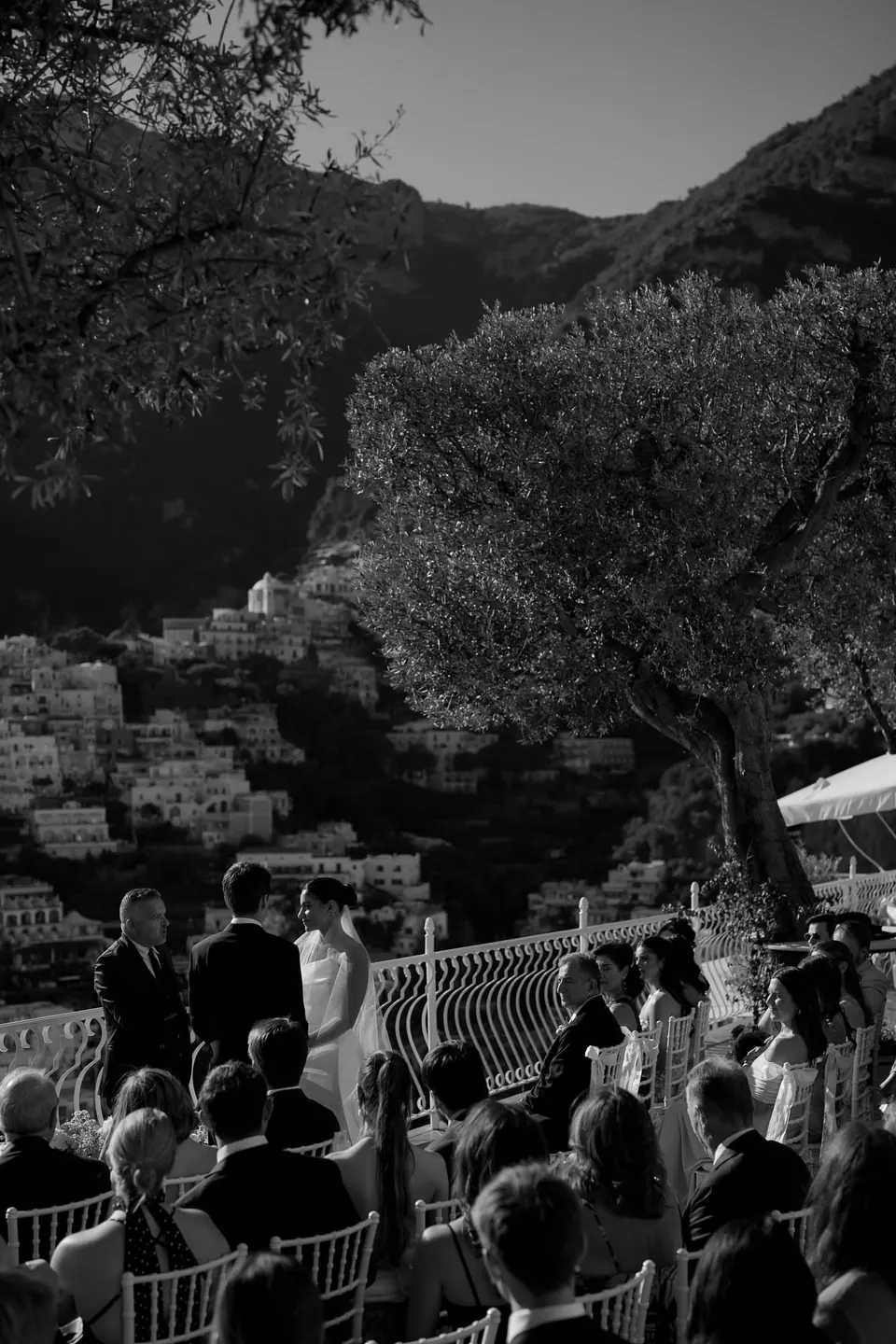 Black and white photo of guests seated at the ceremony on the terrace, trees around them.