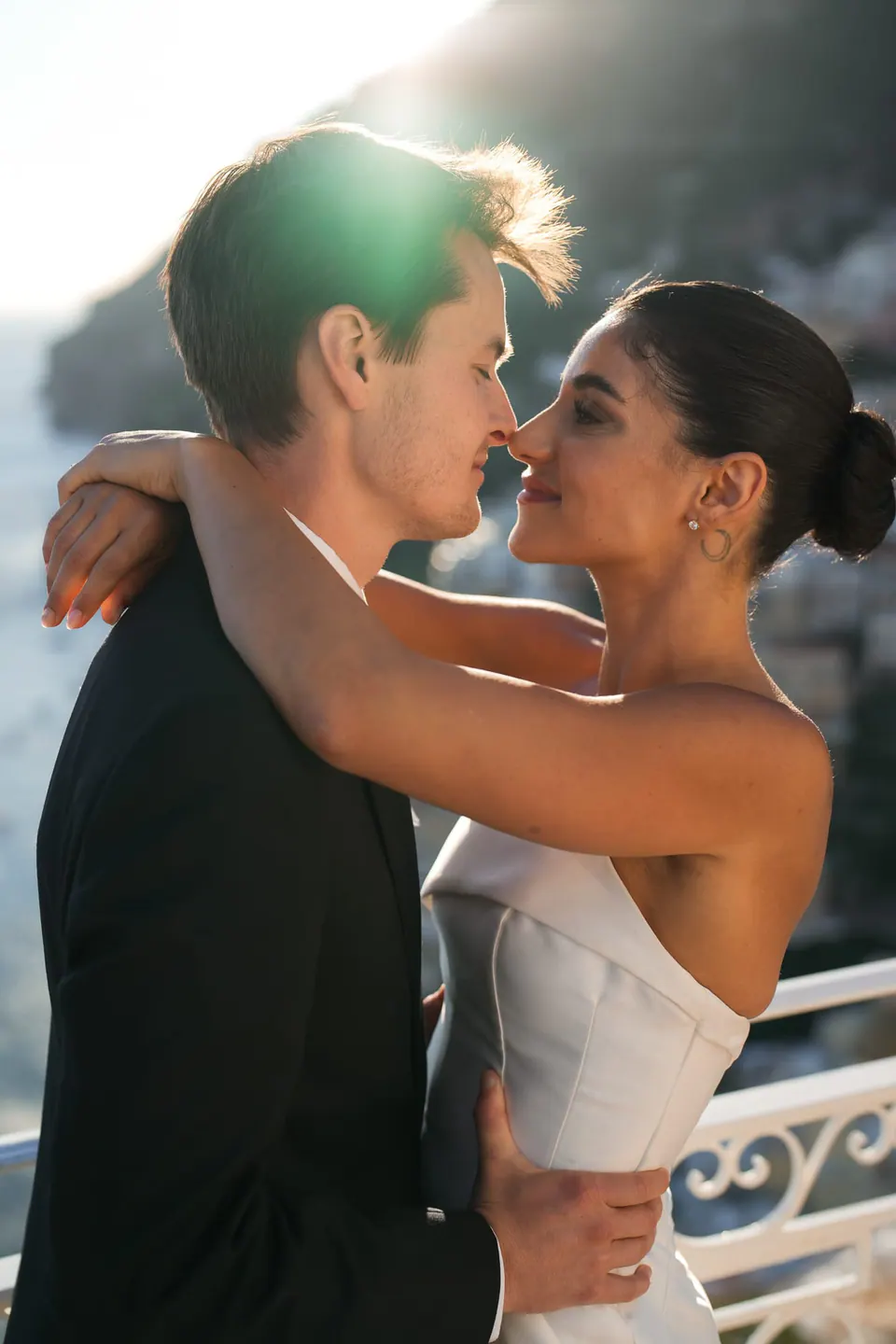 Bride and groom embracing in the golden light above the sea.
