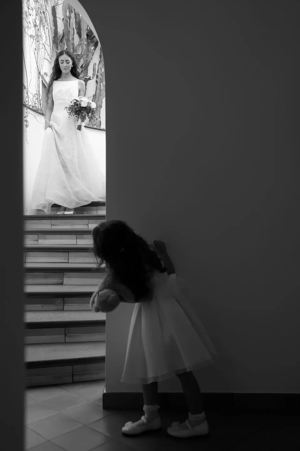 Black and white photo of a little girl on the stairs, the bride behind her.