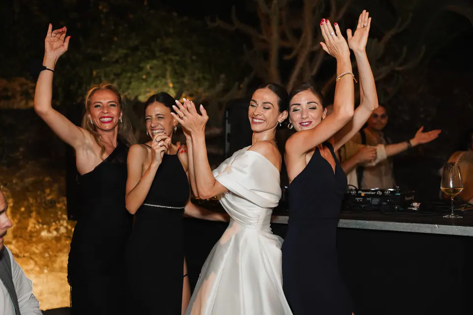 La sposa e le amiche ballano con le braccia alzate di sera.
