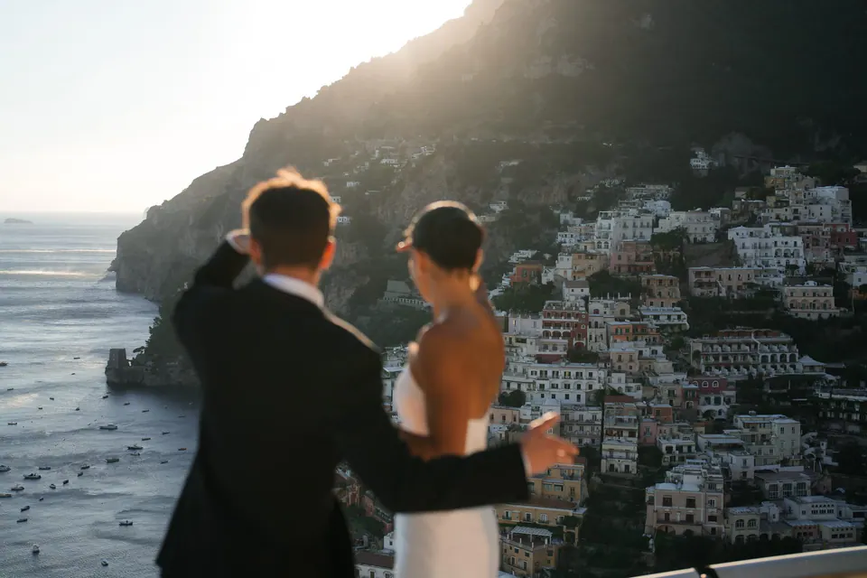 Bride and groom at the railing in silhouette against Positano at sunset.