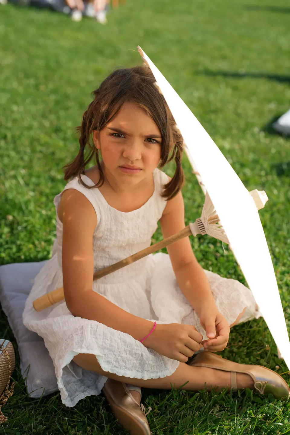 A little girl sitting on the grass with a white parasol