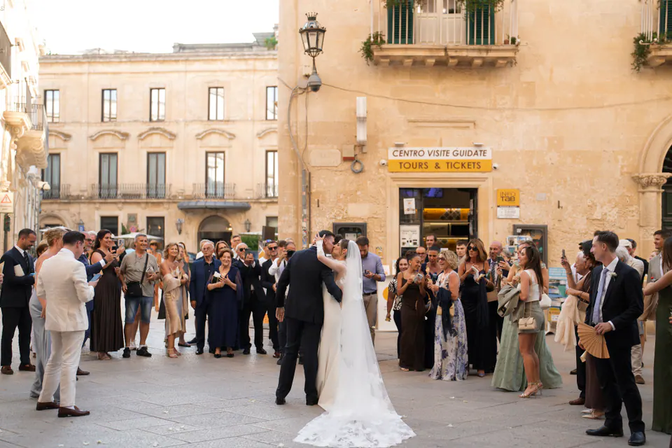 Gli sposi che si baciano in una piazza di Lecce, circondati dagli invitati dopo la cerimonia nella Basilica di Santa Croce.