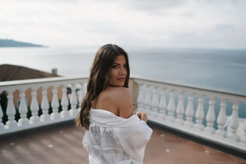 Bride in an off-shoulder robe looking into the distance in morning light.
