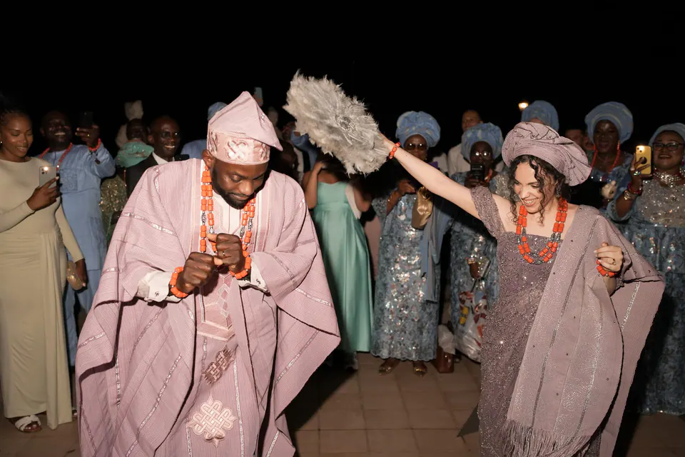 Los novios con traje nigeriano rosa entran bailando entre los invitados por la noche.