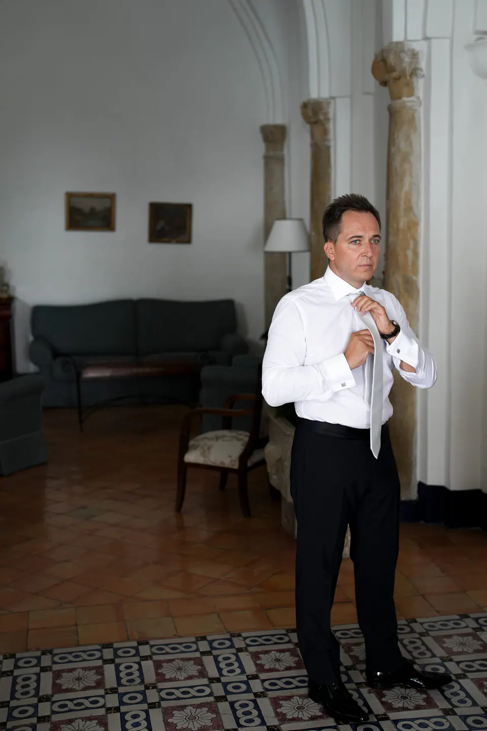 Der Bräutigam knöpft am Fenster des Belmond Hotel Caruso sein Sakko zu.