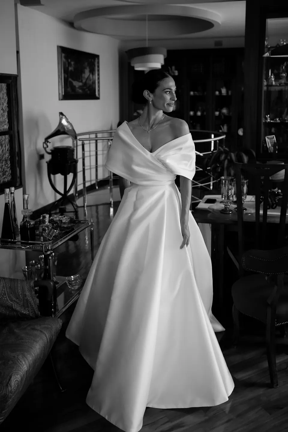 Foto in bianco e nero della sposa in piedi in soggiorno, lo strascico disteso dietro.
