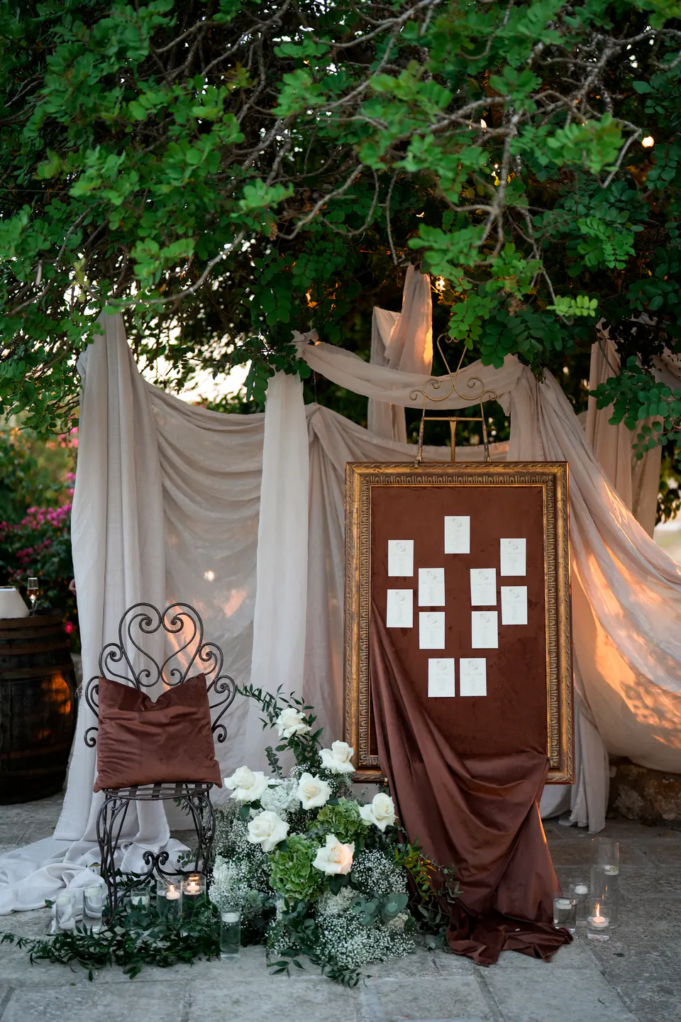 Il tableau in una cornice dorata, tessuti drappeggiati, candele e fiori bianchi sotto gli alberi.