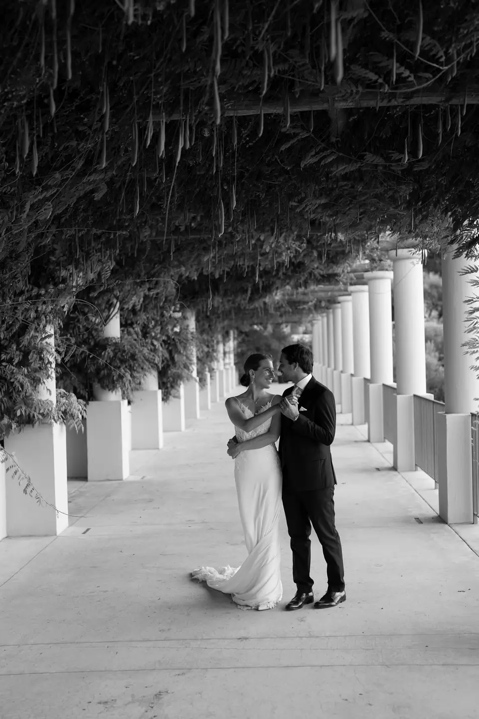 Black and white photo of the couple under a long pergola.