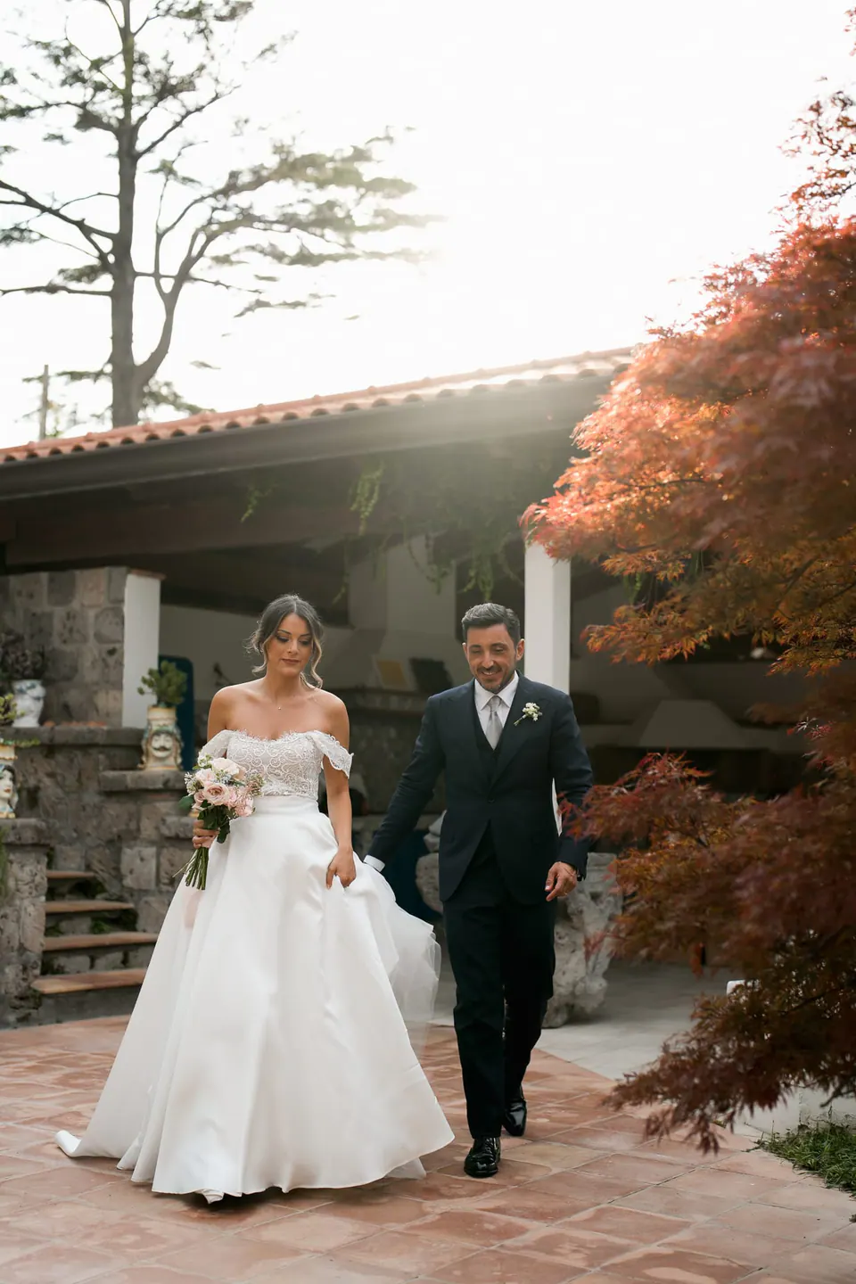 Bride and groom walking out from the villa porch under a red maple