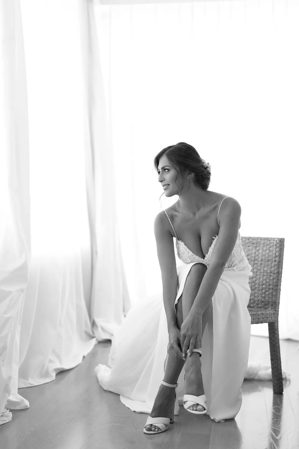 Foto in bianco e nero della sposa che indossa le scarpe vicino alla finestra.