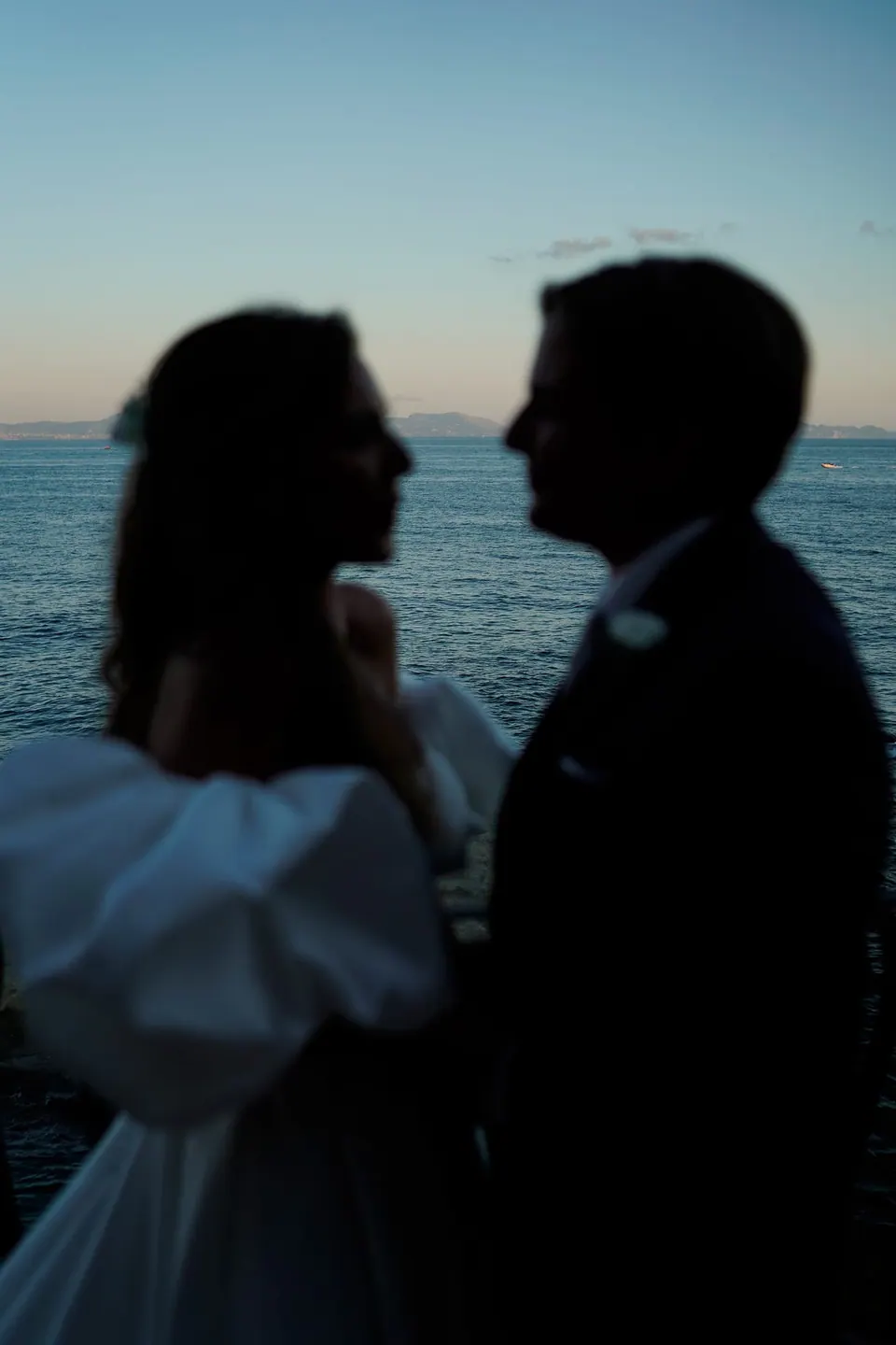 Silhouettes of the bride and groom against the sea at dusk.
