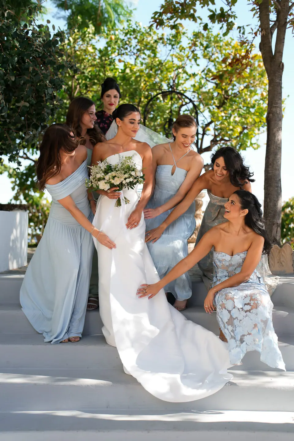 Bridesmaids in powder blue arranging the bride's train on the white steps.