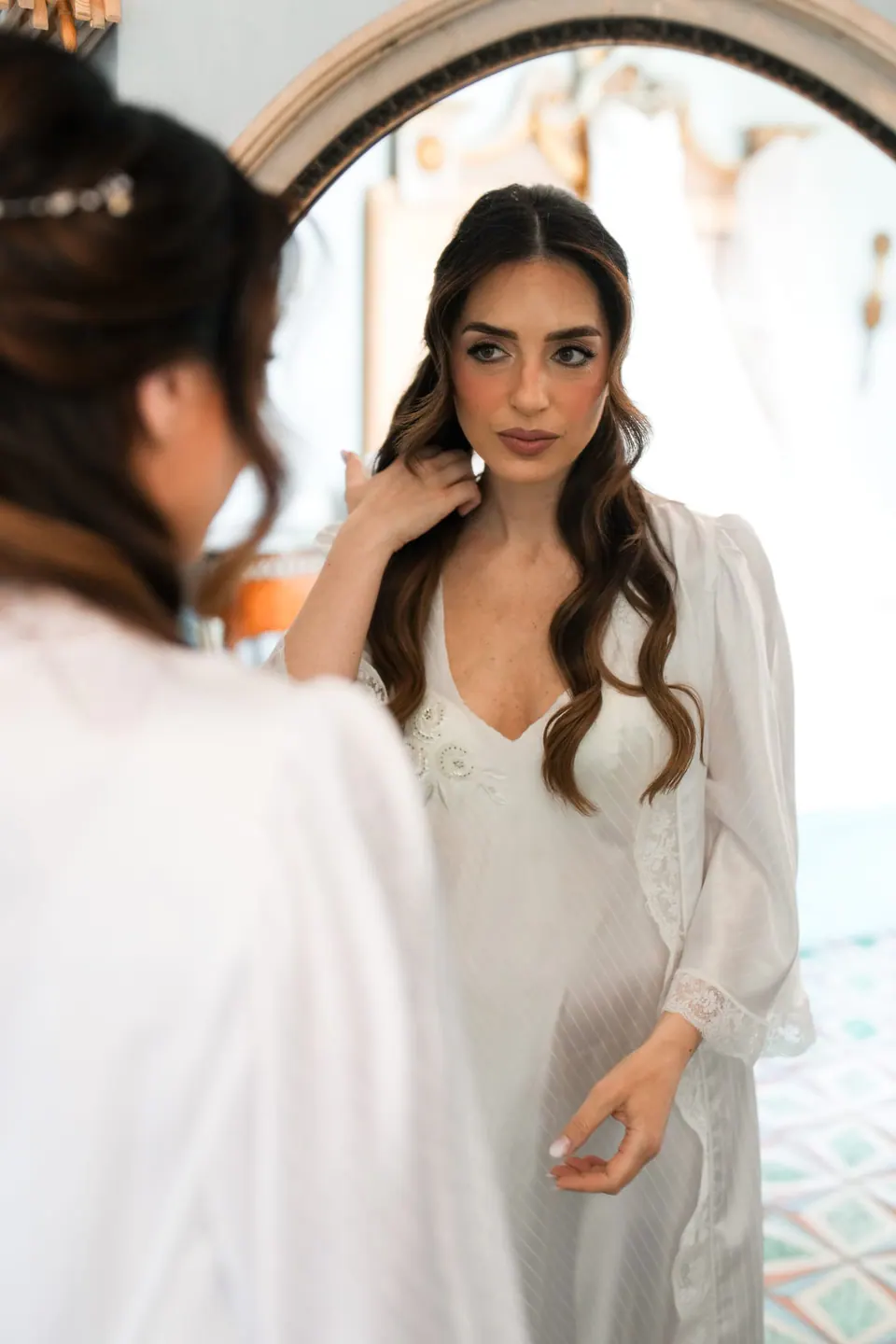 La novia en bata junto a una ventana en arco.