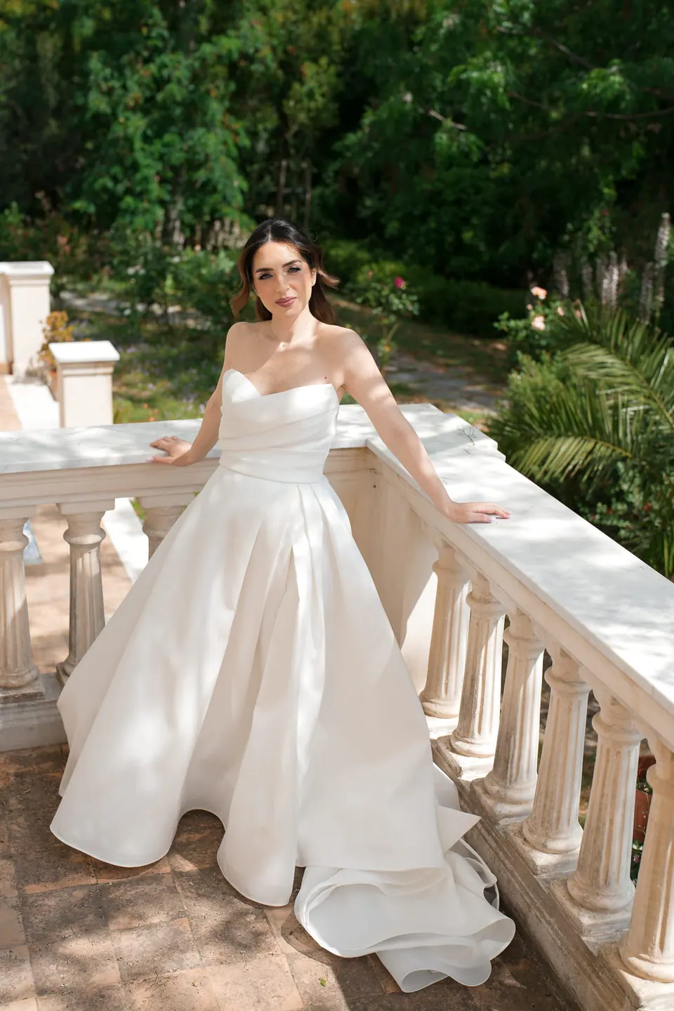 La novia vestida en una balaustrada blanca del jardín.