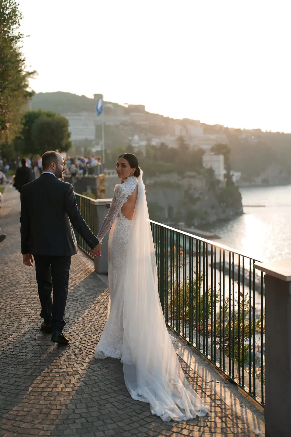 Bride and groom walking along a railing above the sea at sunset