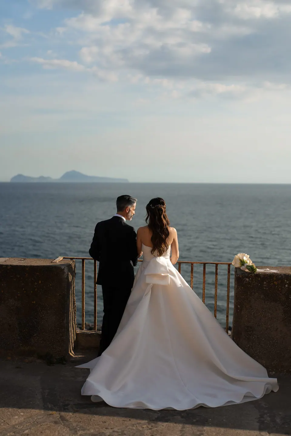 Los novios de espaldas en una barandilla sobre el mar.