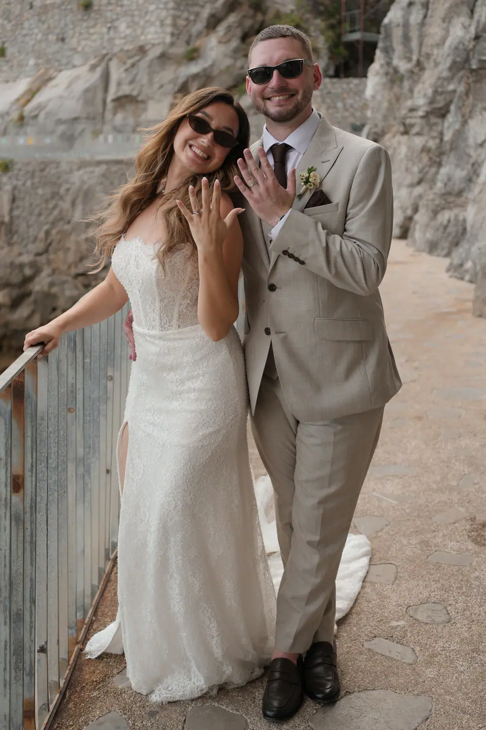 Couple laughing on a cliffside path, the bride showing her ring.
