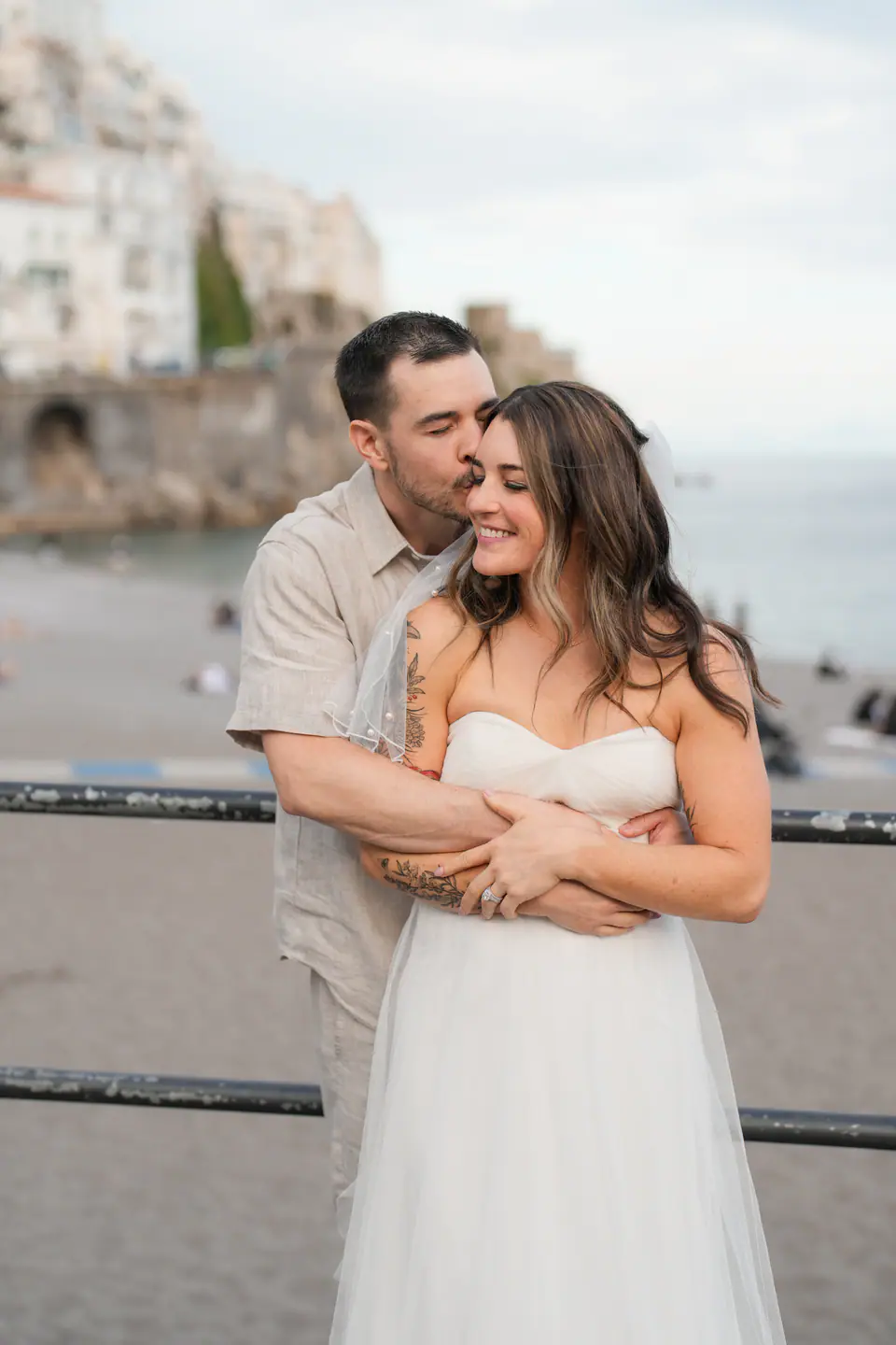 Groom hugging the bride from behind at the seafront railing in Amalfi.