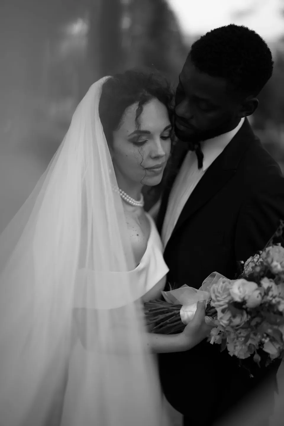 Abrazo cercano en blanco y negro, con el velo enmarcando a la pareja y el ramo.