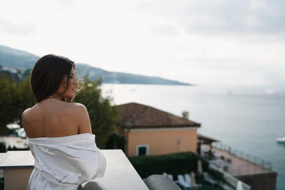 Bride in her robe against the sea view while getting ready.