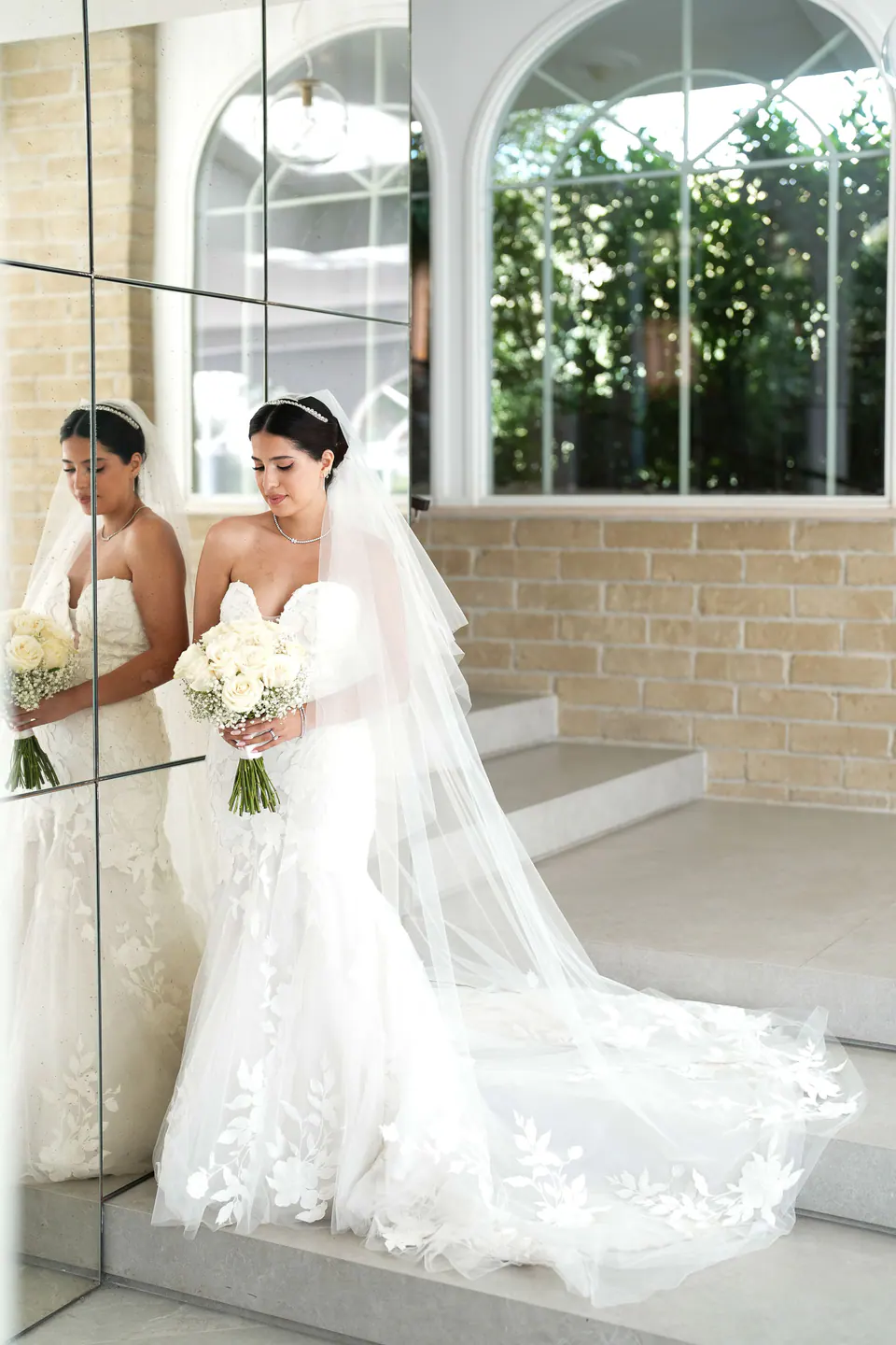 La mariée reflétée dans un miroir, voile et traîne de dentelle étalés sur le sol.