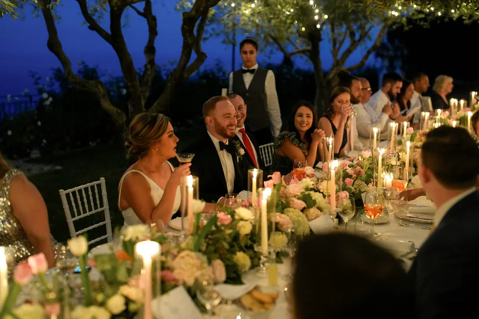 Bride and groom seated at the long candlelit table, enjoying an intimate dinner with guests.