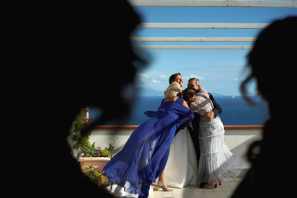 Bride hugging her mother on the terrace, framed by the silhouettes of guests.
