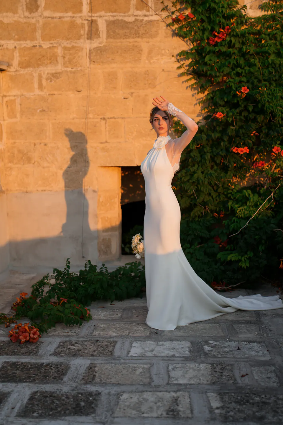 La sposa contro un muro di pietra al sole coperto di bignonia, con la sua ombra sulla pietra.