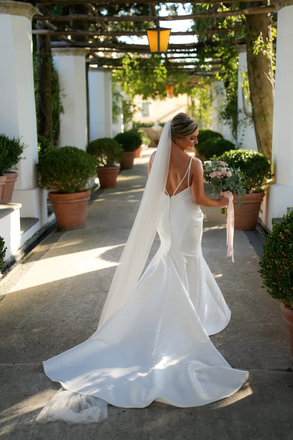 Bride seen from behind walking under the pergola, her train behind her