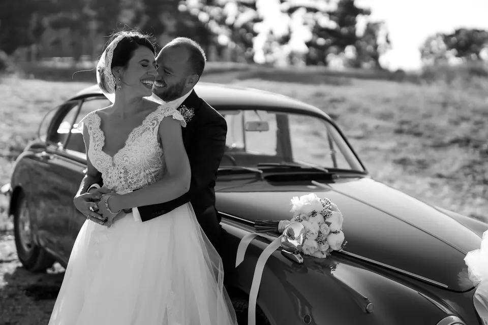 Bride and groom holding each other beside a vintage car in Terrasini, Sicily.