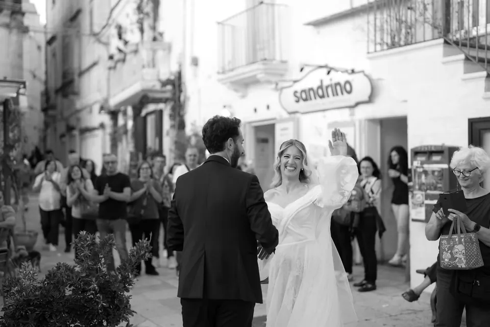 Foto en blanco y negro de los novios saludados por la gente en la calle.