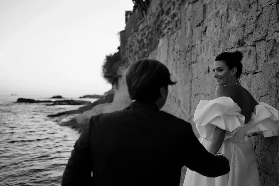Black and white photo of the groom meeting the bride on the rocks by the sea in Marechiaro.