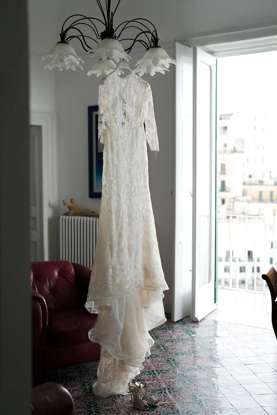 Das Brautkleid hängt an einem Kronleuchter neben einem offenen Fenster.