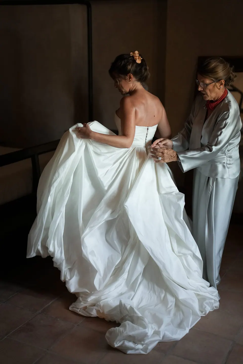 La sposa solleva la gonna mentre un'aiutante sistema l'abito in camera.