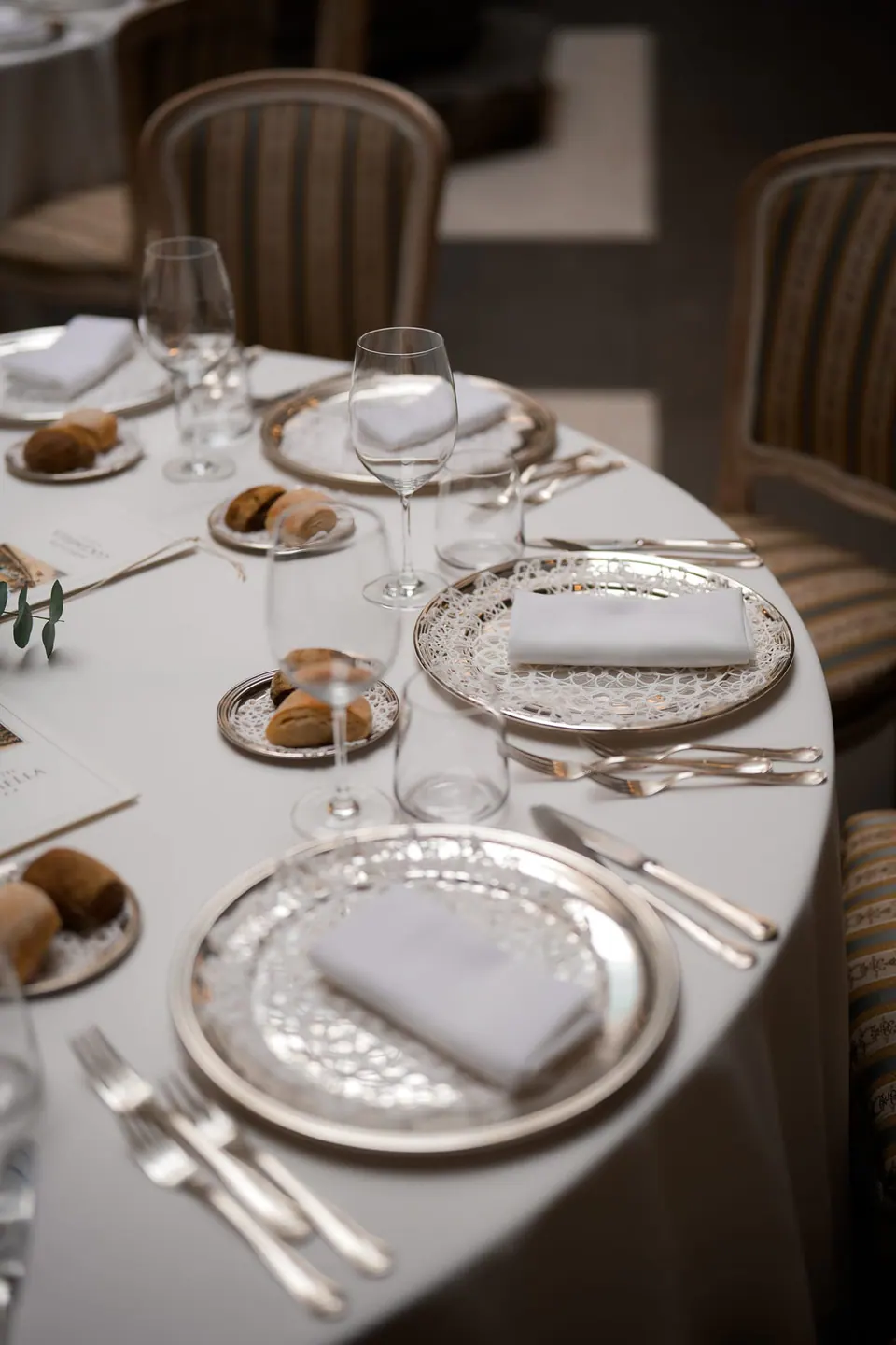 Gedeckter Tisch mit silbernen Platztellern und weißen Servietten.