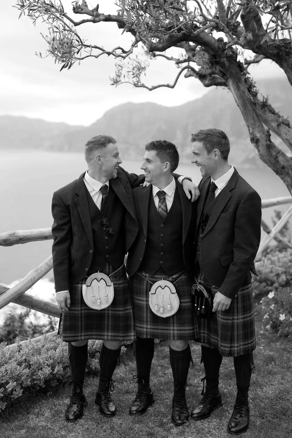 Ritratto in bianco e nero dei testimoni in kilt sotto l'ulivo, la costa alle spalle.