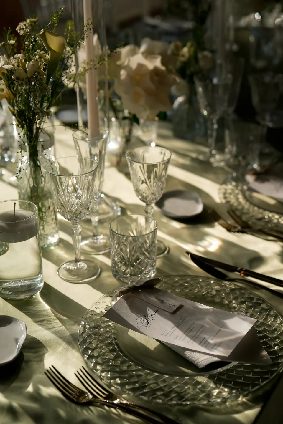Table setting with sage green linen, cut crystal glasses and white flowers.