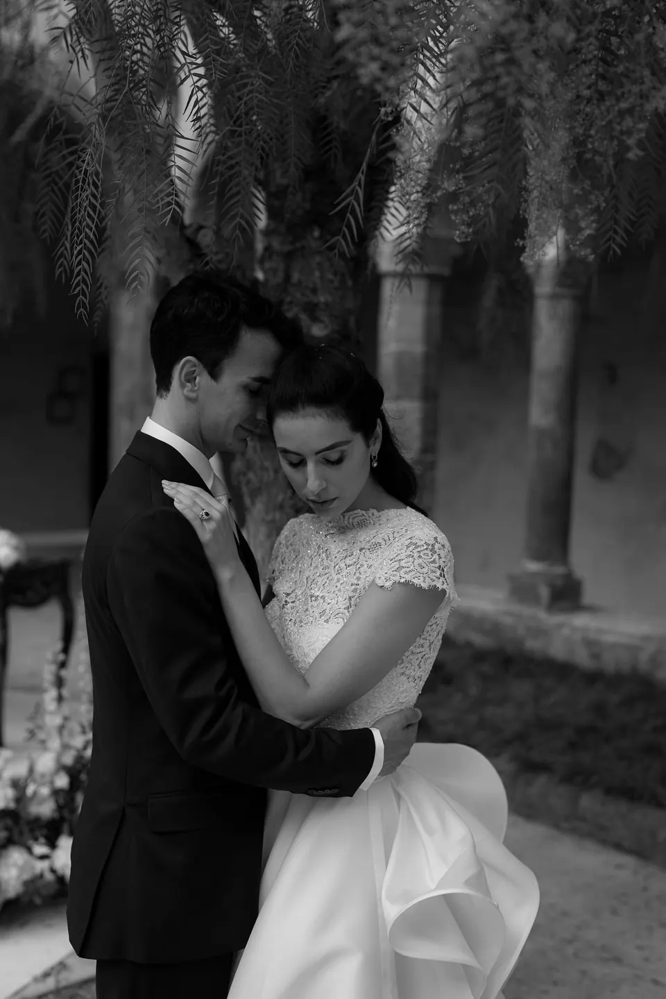 Black and white photo of bride and groom embracing under the palms
