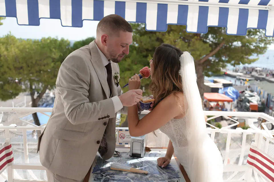 Groom feeding the bride a spoonful of gelato under a striped awning in Positano.