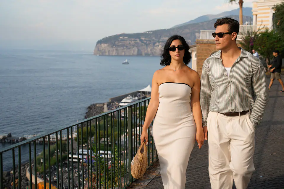 Couple walking along a terrace above the sea, the cliffs of Sorrento behind.