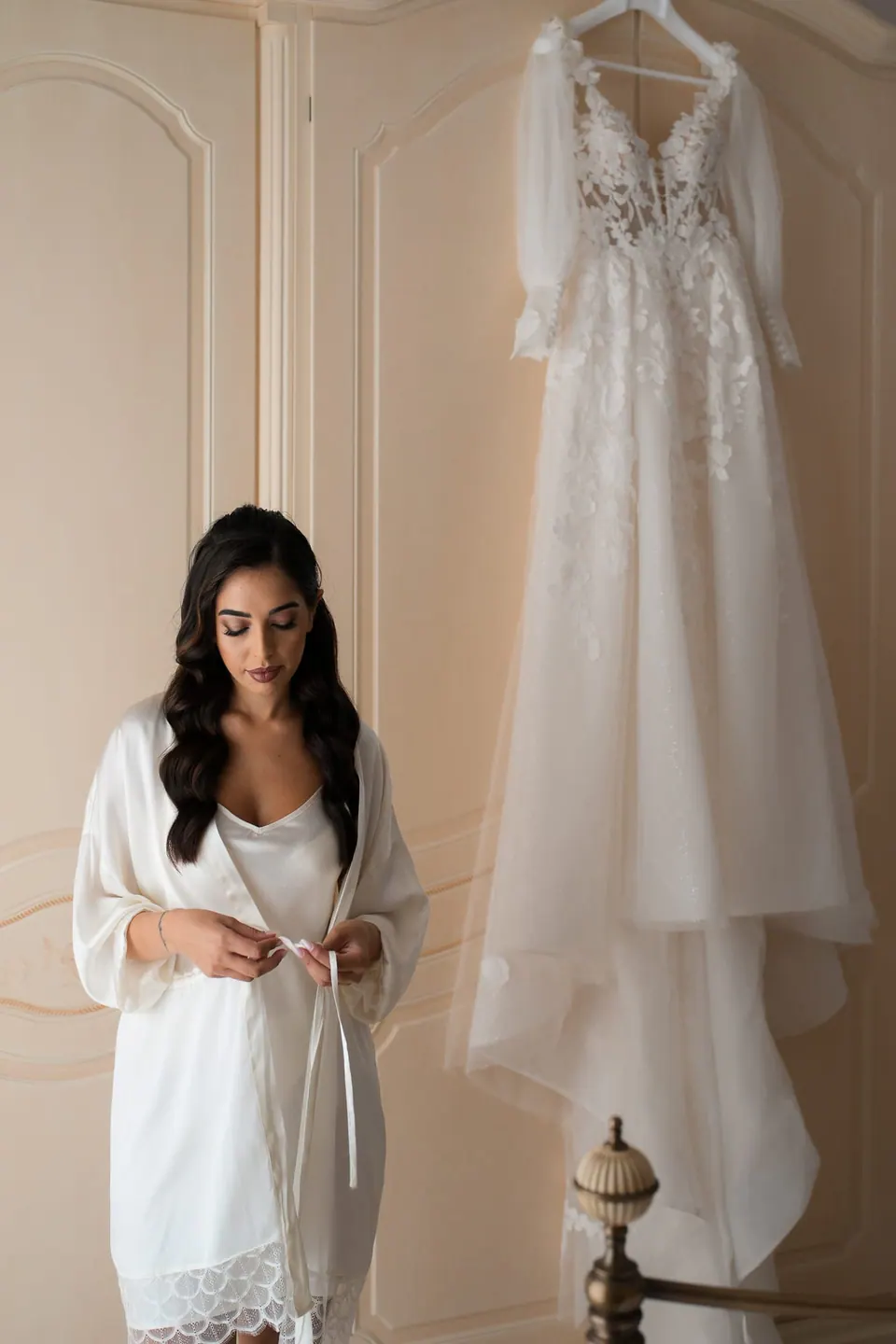 Bride in her robe standing beside her wedding gown before getting dressed.