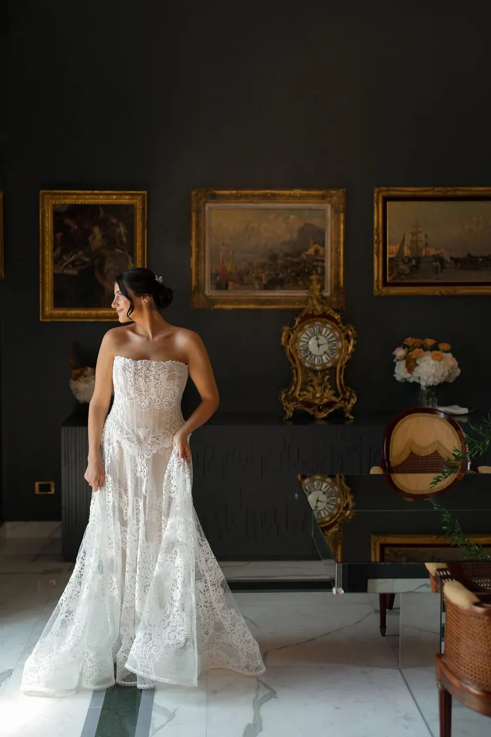 Die Braut im Spitzenkleid zwischen alten Gemälden im dunklen Salon.
