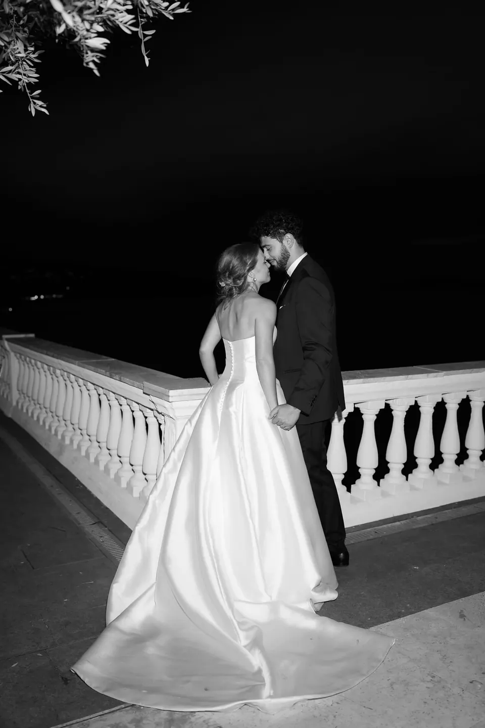 Schwarzweißfoto: Das Paar küsst sich nachts an der weißen Balustrade.