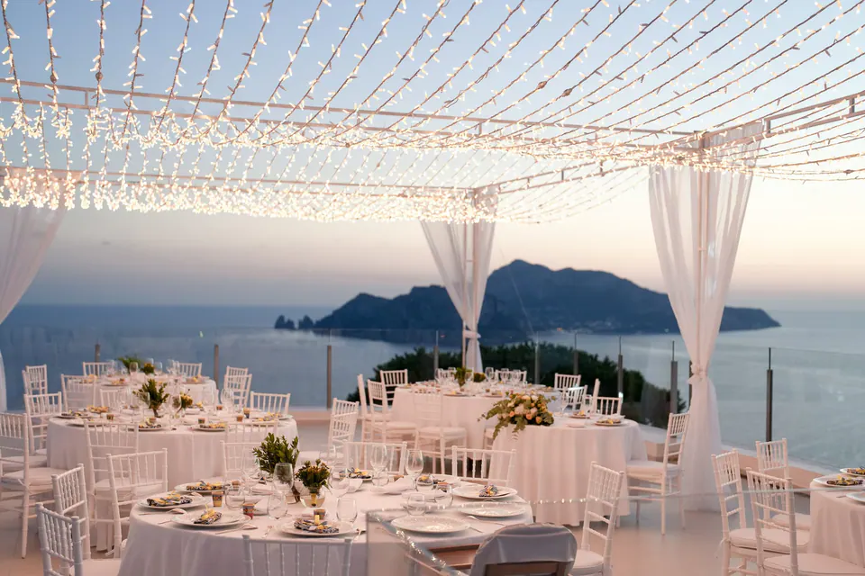 Tavoli del ricevimento sotto un cielo di lucine e tende bianche al Relais Blu, Capri al crepuscolo.