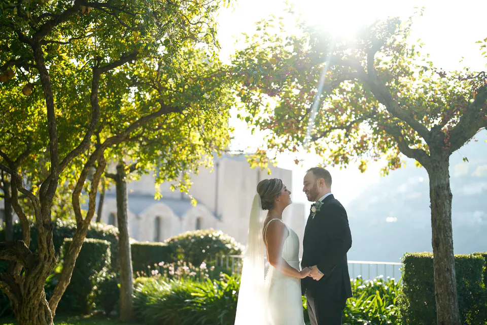 Bride and groom facing each other in the garden, backlit among the trees